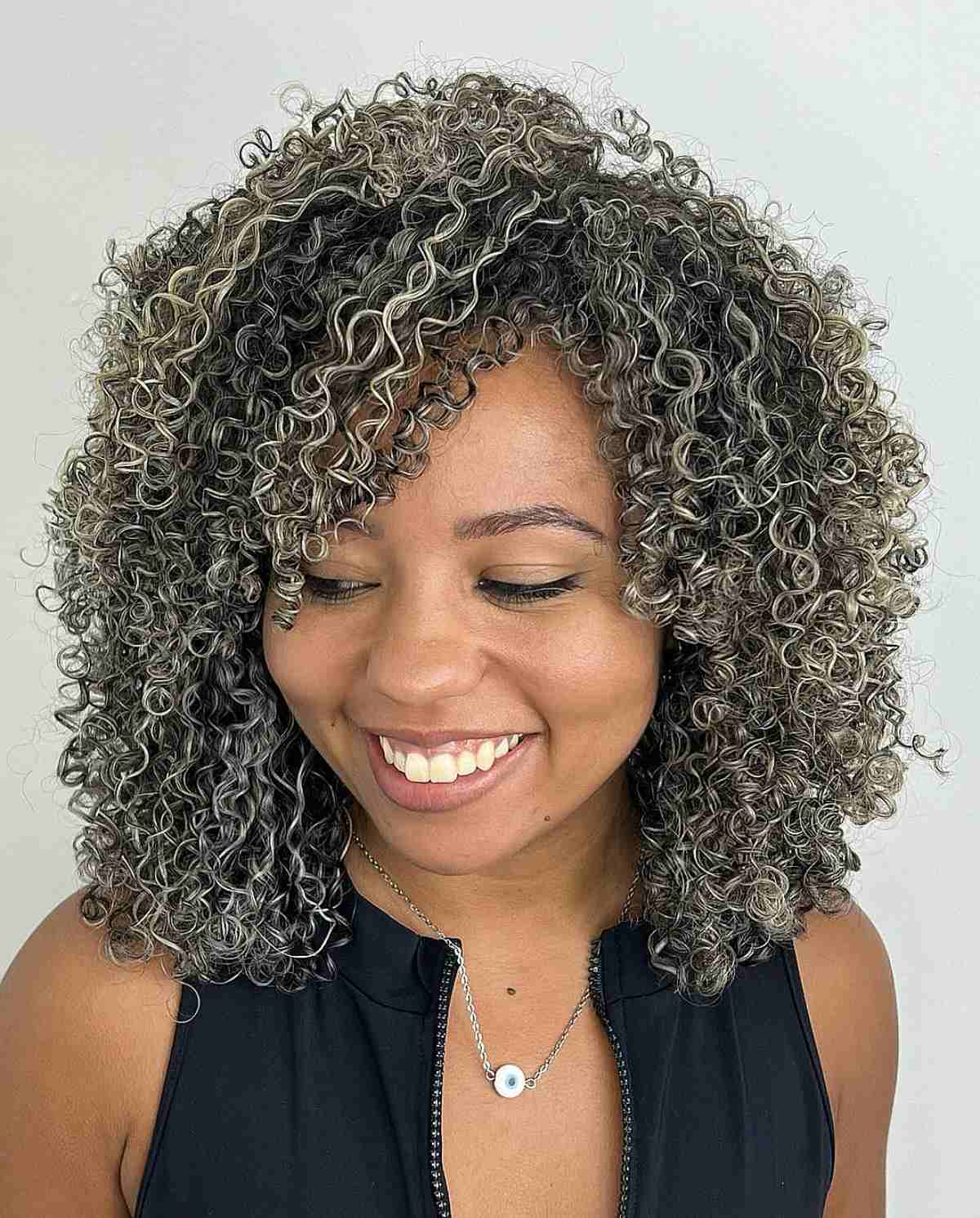 A woman with a Cadō cut featuring layered ringlets and grey highlights that define the curls and add volume.