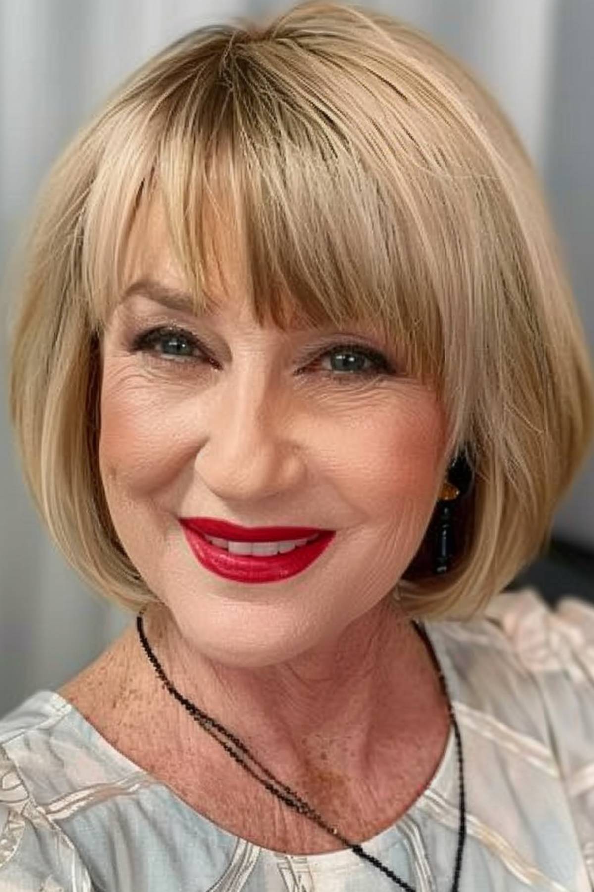 Woman over 60 showcasing a haircut with soft bangs and subtle layers that enhance her radiant look.