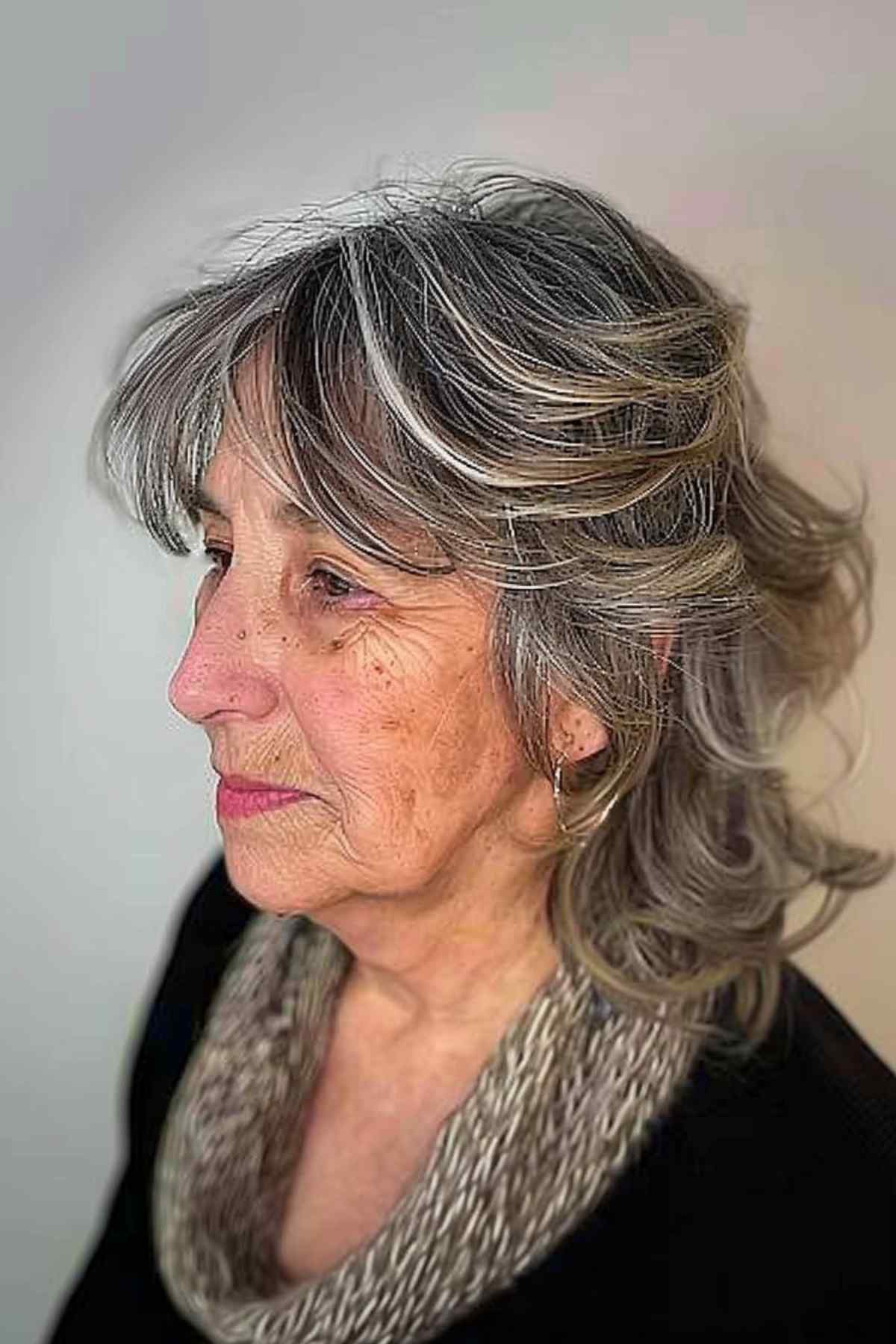 A senior woman with an undone shag haircut and casual bangs that enhance her natural wavy hair, offering an easy-to-maintain, textured style.