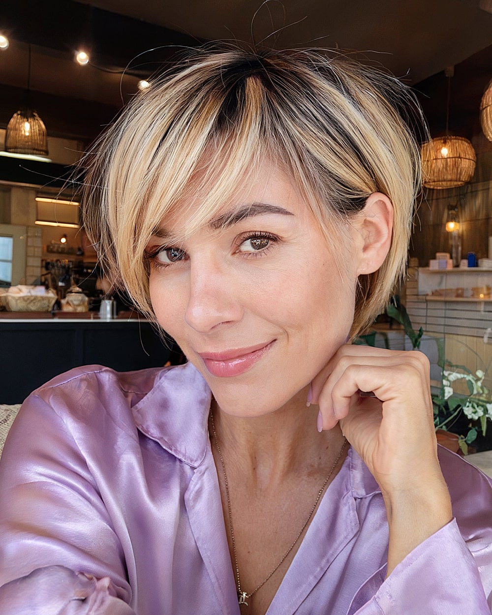 Blonde pixie bob with dark root shadow and piece-y bangs for women over 40