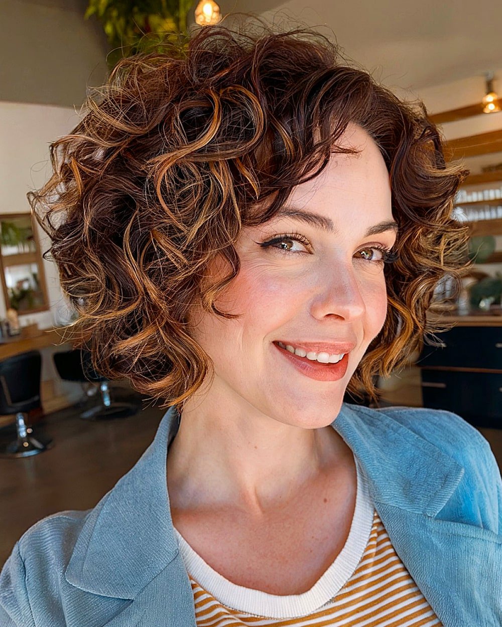 Choppy stacked curly bob with layered ends and caramel highlights