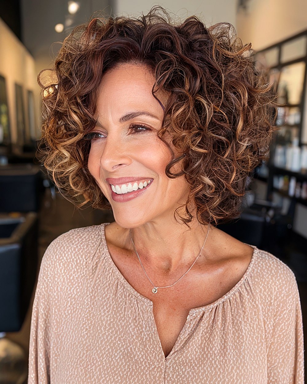 Inverted stacked curly bob haircut with voluminous curls and darker root dimension