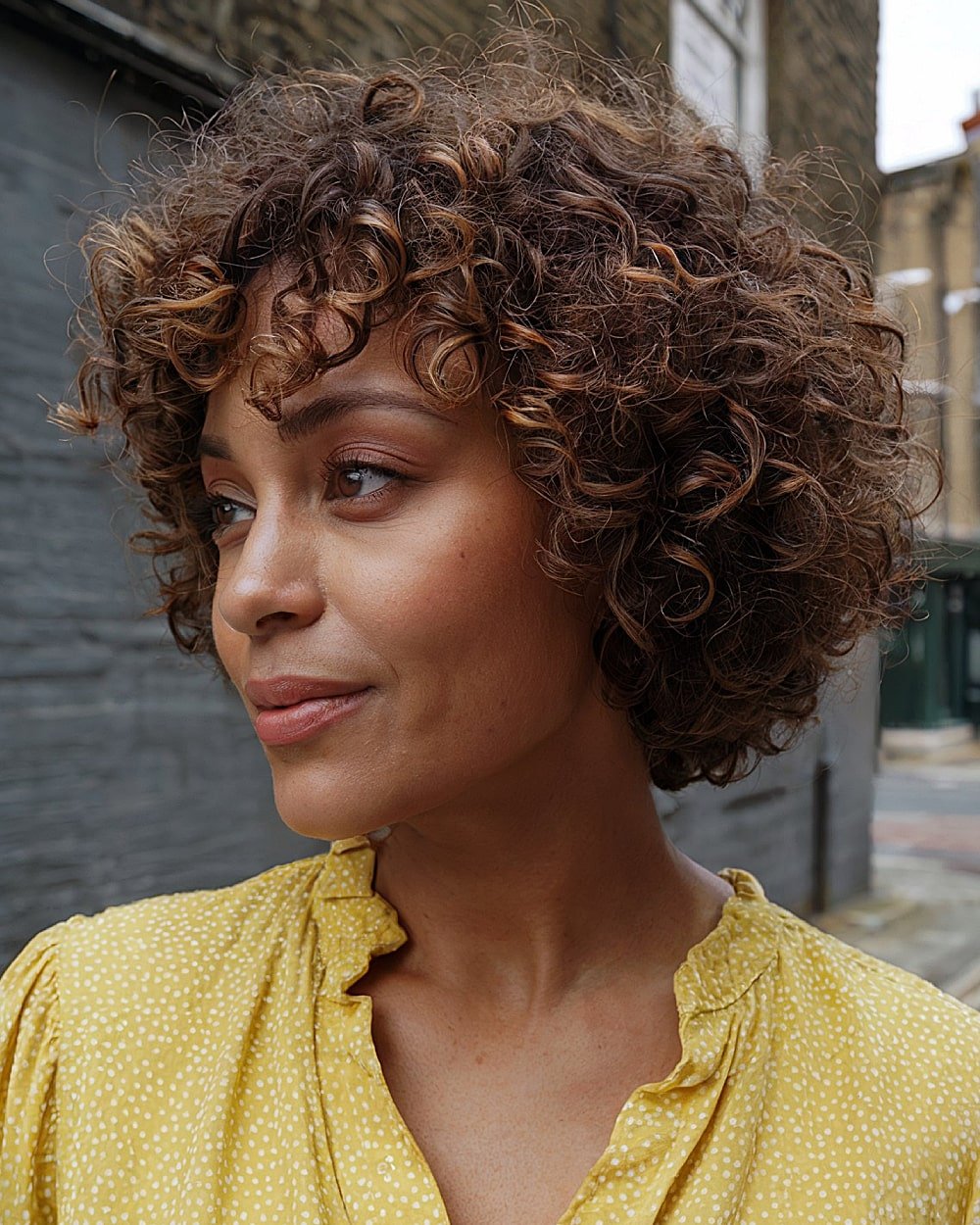 Naturally curly stacked bob with tight spirals and warm highlights for coily textured hair